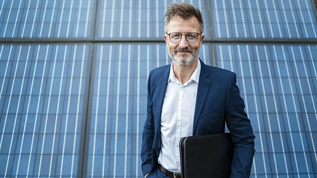 Portrait of smiling businessman holding folder standing in front of solar panels