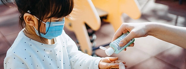 Young mother squeezing hand sanitizer onto little daughter’s hand in the playground to prevent the spread of viruses