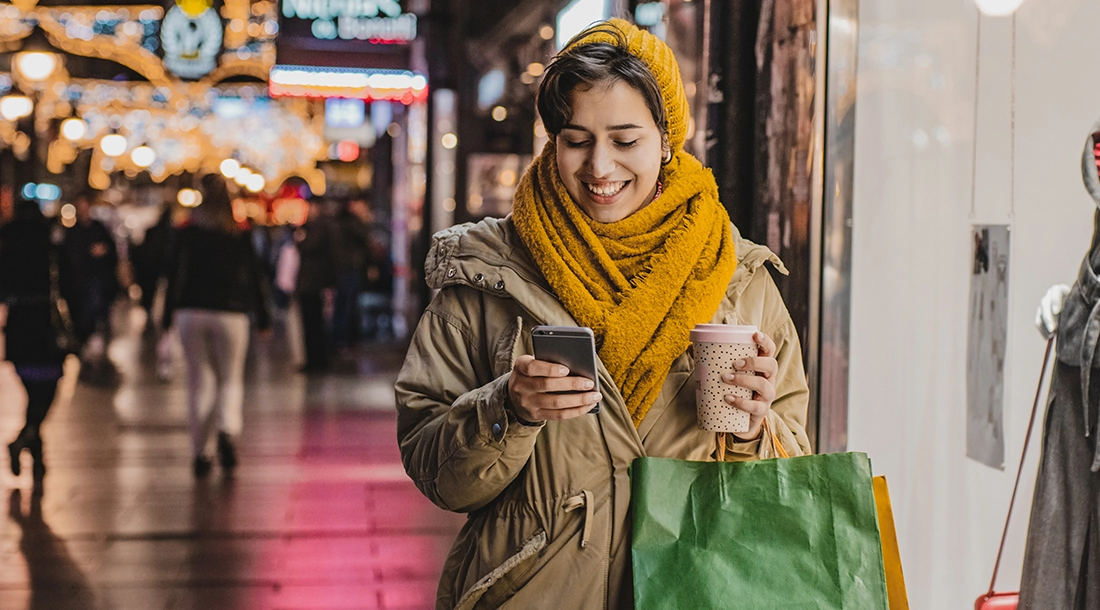 Happy woman in holiday shooping holding mobile phone